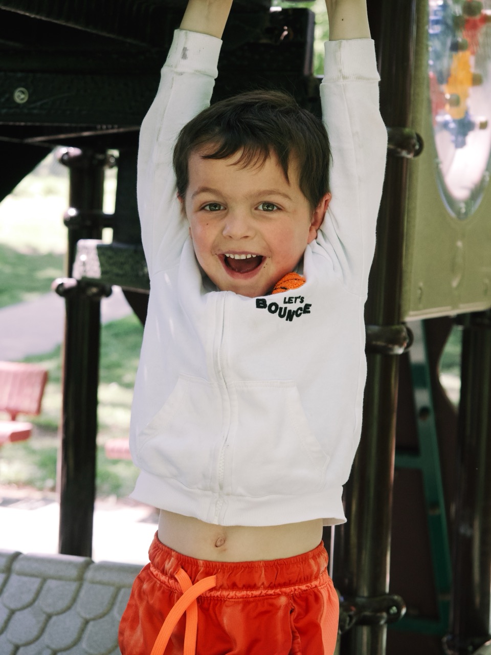 Lifestyle family session — boy hanging from playground bars with a huge smile